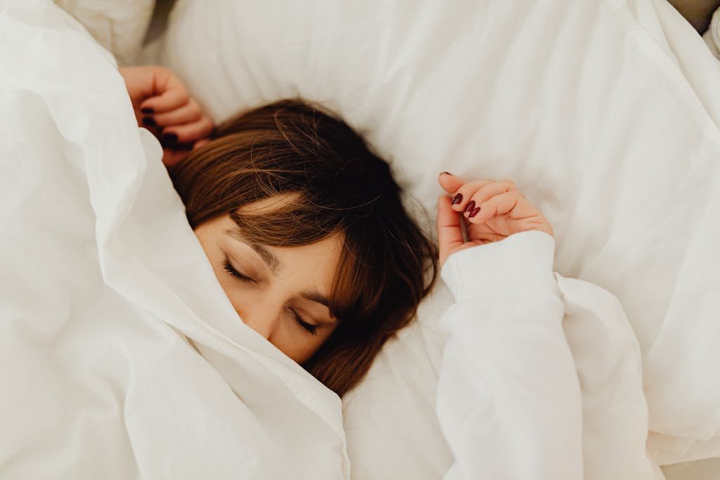 A woman peacefully sleeping under a white blanket in a cozy bed setting.