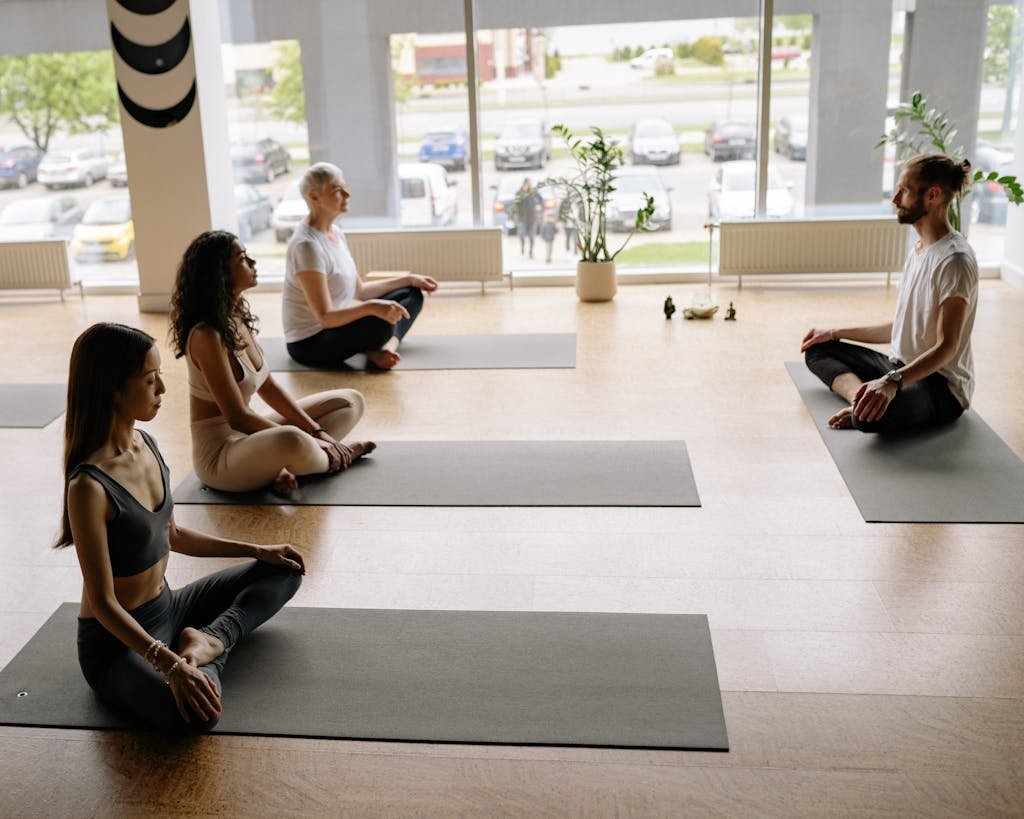 Four people meditating on yoga mats in a bright studio promoting wellness and relaxation.
